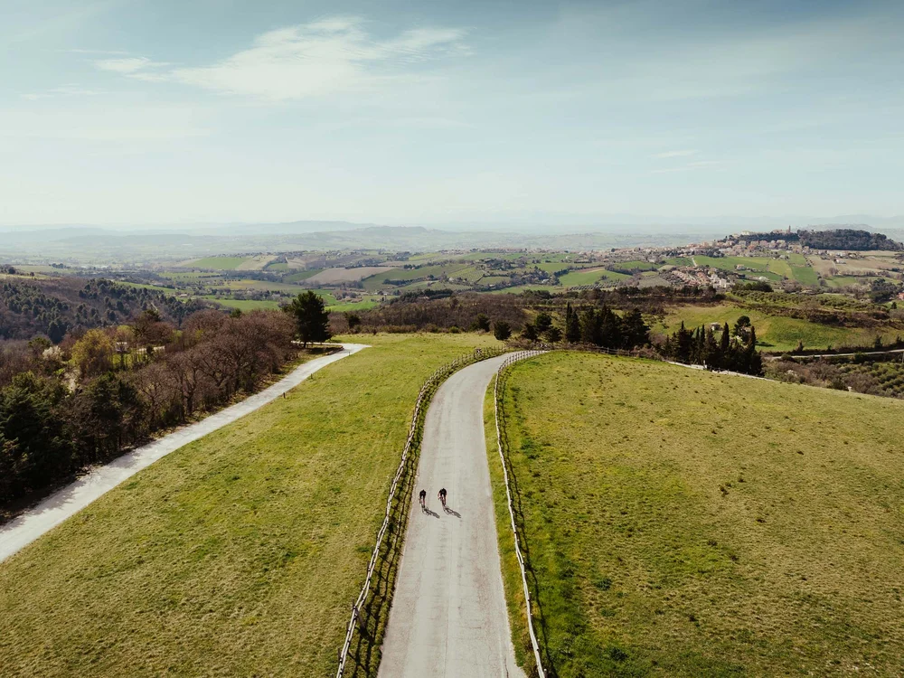 Una vacanza in gravel bike nelle Marche Vista aerea di due ciclisti che pedalano su una strada tra colline verdi