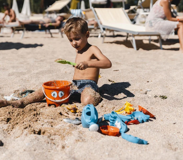 Un resort sul Conero con spiaggia privata Bambino che gioca con la sabbia e secchiello arancione sulla spiaggia.