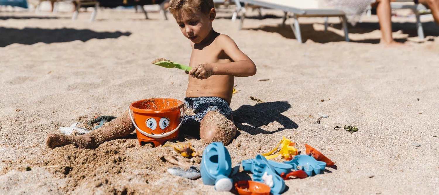 Un family hotel al Conero? Meglio un resort! Bambino che gioca con la sabbia e secchiello arancione sulla spiaggia.