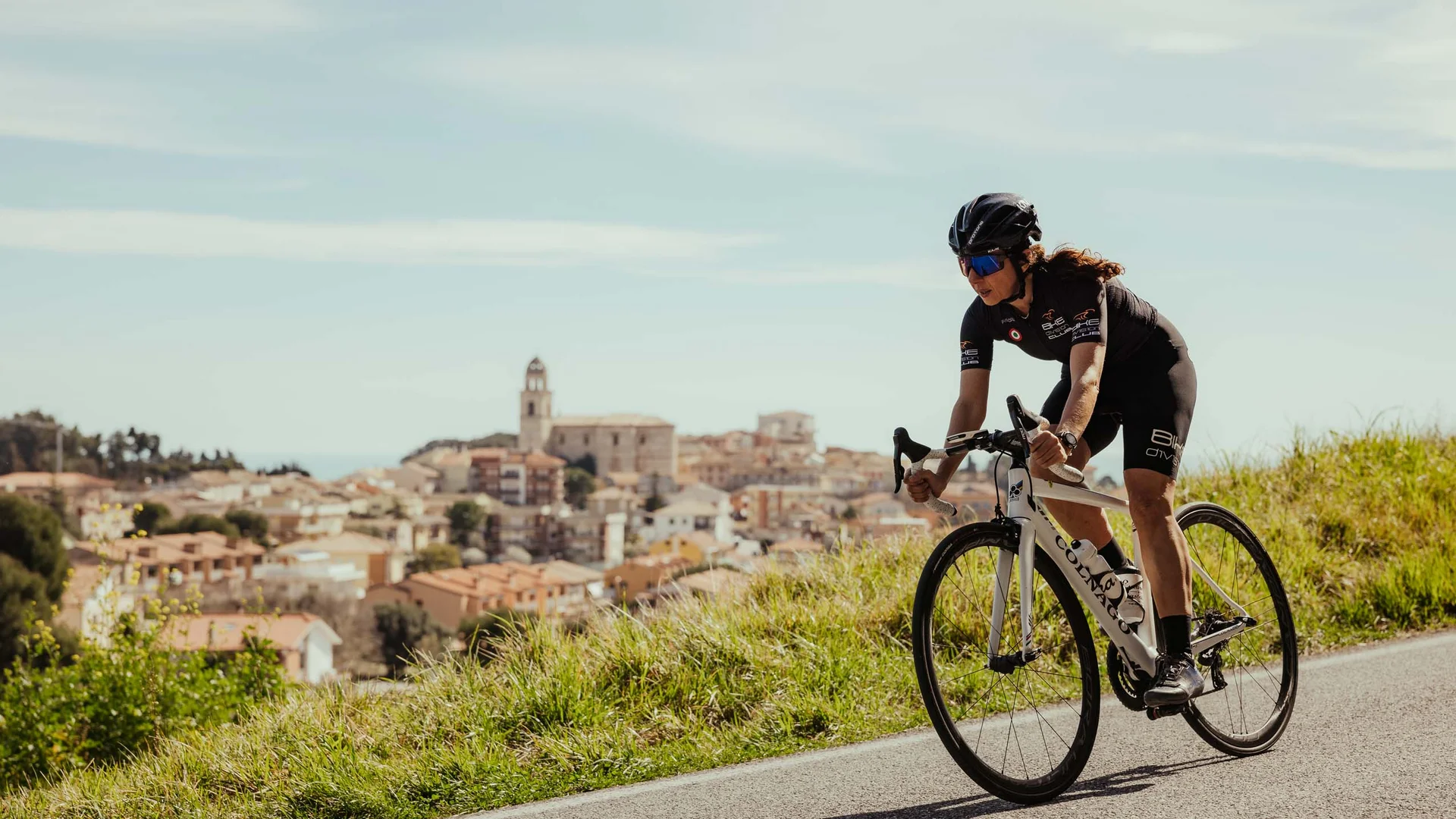 Dai monti al mare: le vostre avventure nelle Marche Ciclista donna in abbigliamento da corsa su strada panoramica collinare