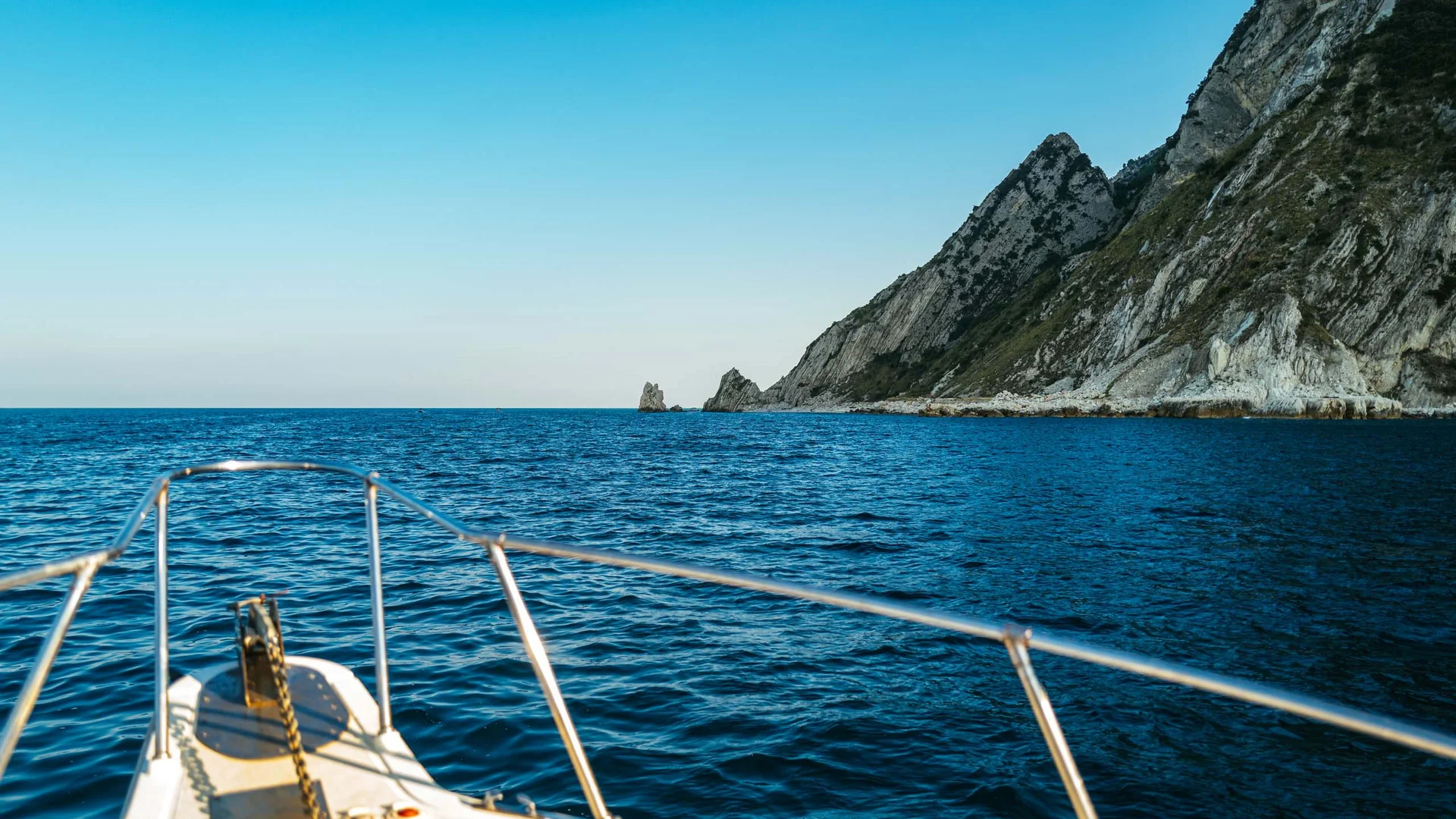 Escursioni in barca al Conero e molto altro Vista dalla prua di una barca verso una scogliera rocciosa nel mare blu