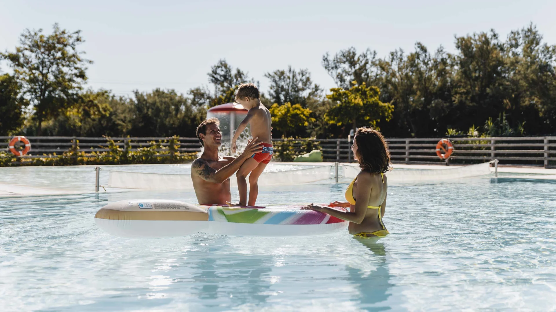 Villaggio nelle Marche sul mare con piscina Famiglia felice in piscina con bambino su un gonfiabile colorato