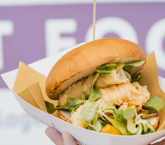 Food truck & Pizzeria a Potenza Picena Panino con pesce fritto e insalata in contenitore di carta tenuto a mano