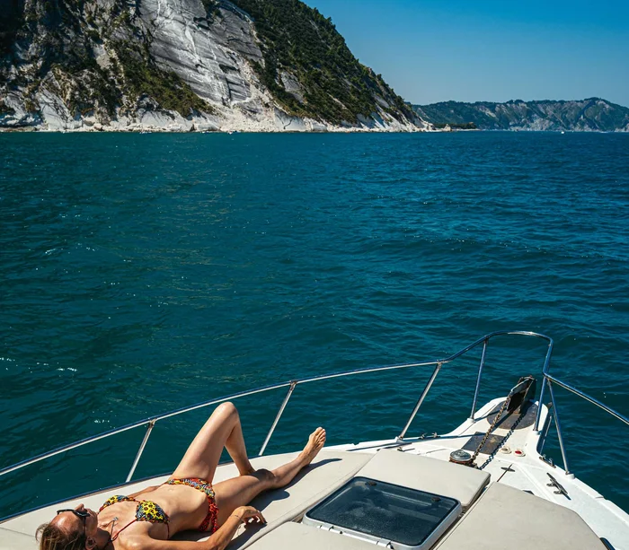 Escursioni in barca al Conero e molto altro Donna in bikini sdraiata a prendere il sole sulla prua di una barca in mare