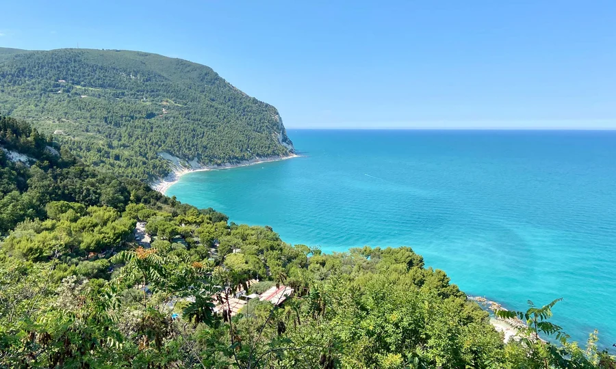 Resort al mare: pronti per un’escursione sul Conero? Costa verde con mare turchese e cielo azzurro limpido in una giornata soleggiata