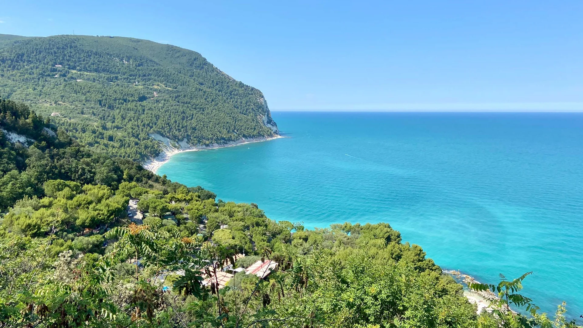 Spiaggia Urbani: la mezzaluna di Sirolo Costa verde con mare turchese e cielo azzurro limpido in una giornata soleggiata