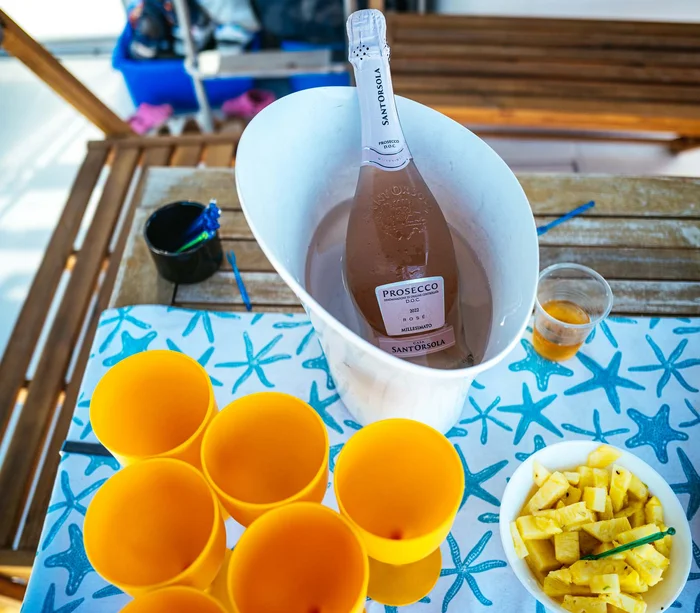 Escursioni in barca al Conero e molto altro Bottiglia di Prosecco in secchiello con bicchieri gialli e ananas su tavolo