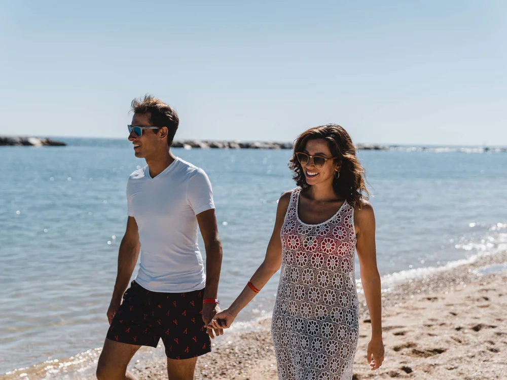 Benvenuti nel nostro resort al Conero Coppia sorridente che cammina mano nella mano sulla spiaggia al sole