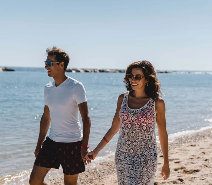Riviera del Conero: le spiagge più belle Coppia sorridente che cammina mano nella mano sulla spiaggia al sole