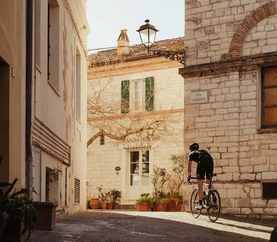 Un family hotel al Conero? Meglio un resort! Ciclista che pedala in una strada di ciottoli in un villaggio storico