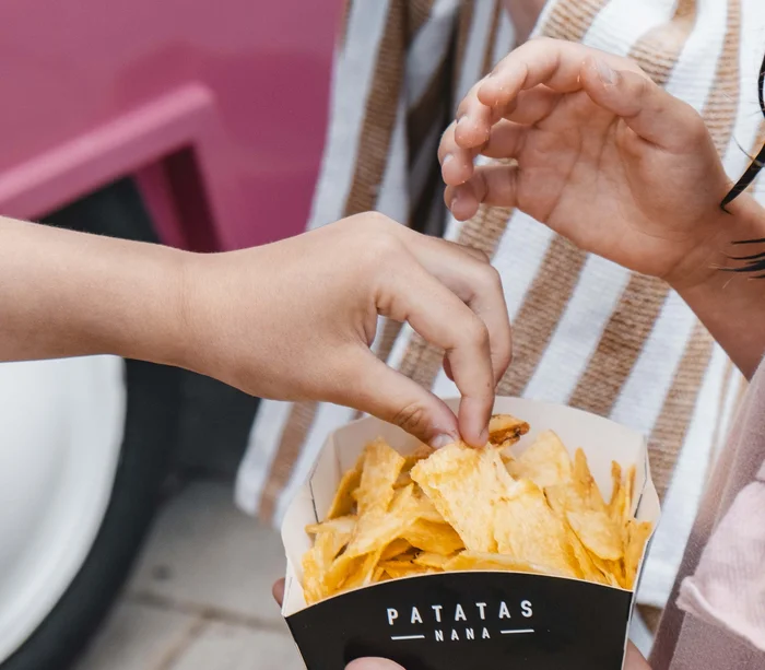 Food truck & Pizzeria a Potenza Picena Mani di bambini che prendono patatine da un contenitore nero con scritta