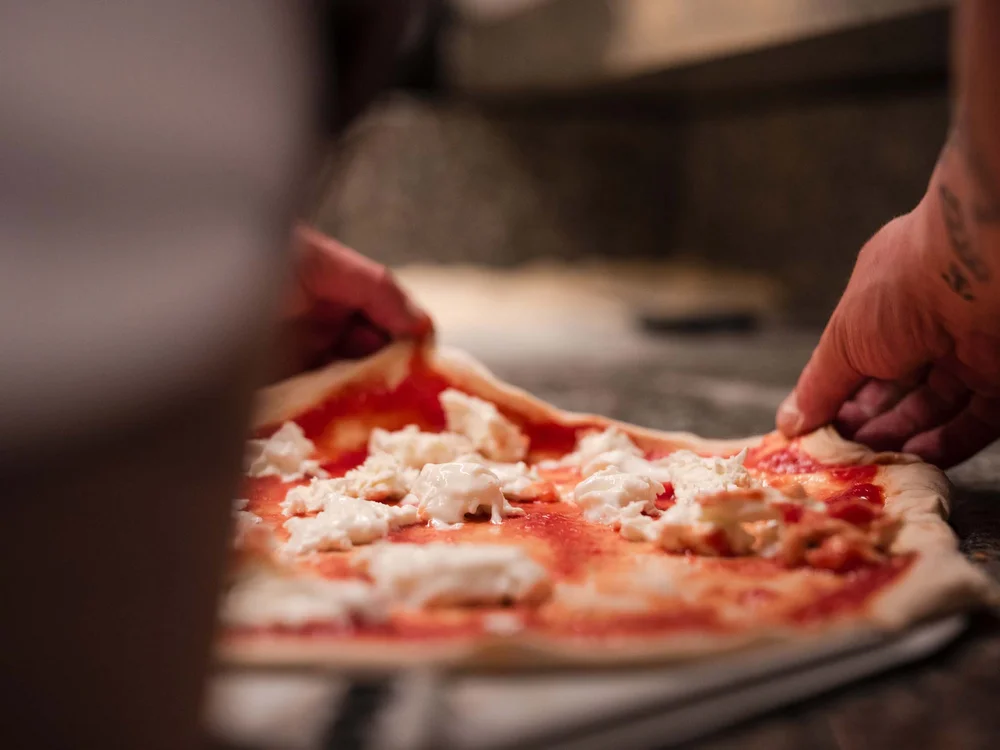 Food truck & Pizzeria a Potenza Picena Mani che preparano una pizza con pomodoro e mozzarella su impasto crudo