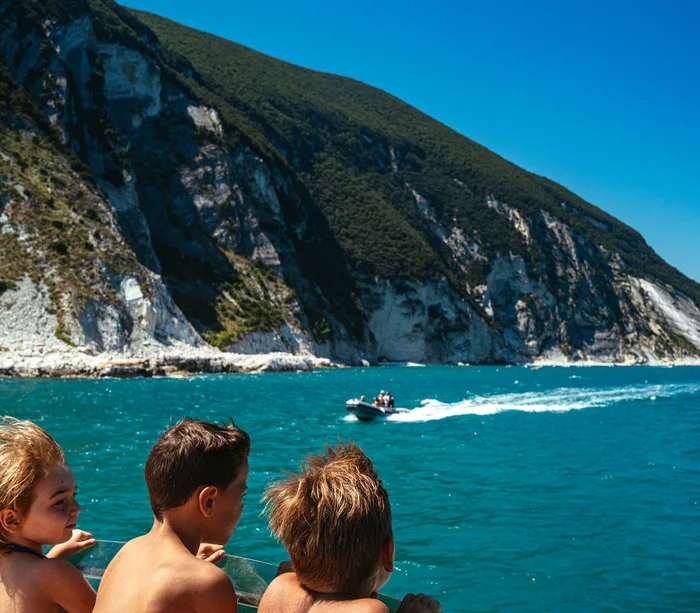 Escursioni in barca al Conero e molto altro Tre bambini su una barca guardano il mare e una barca veloce vicino alla costa rocciosa