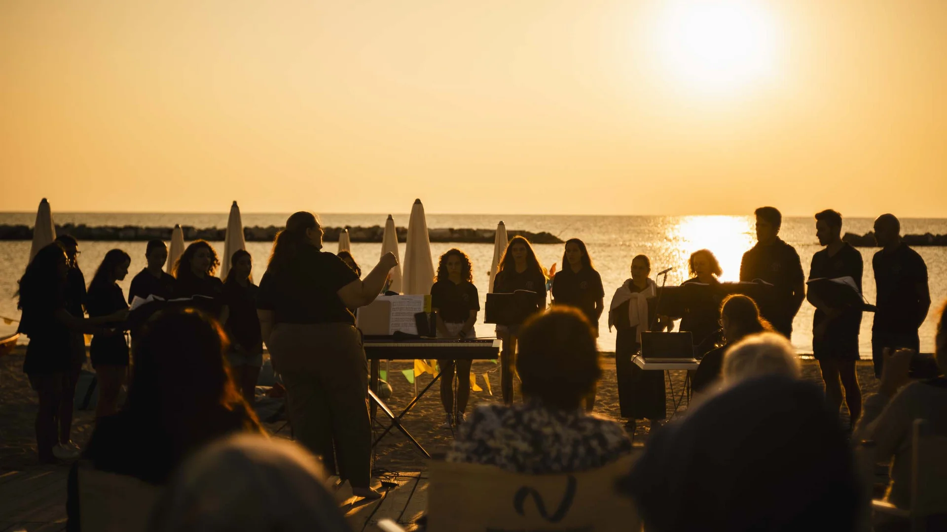 Gli eventi al Natural Village Resort Coro che canta sulla spiaggia al tramonto con direttore d'orchestra e pubblico