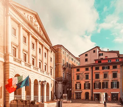 Una vacanza in gravel bike nelle Marche Piazza con il Teatro delle Muse e edifici storici sotto un cielo azzurro.