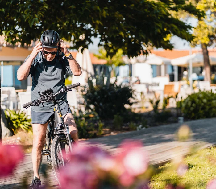 Vacanza in e-bike nelle Marche Uomo che indossa un casco e si prepara per andare in bici in un parco soleggiato