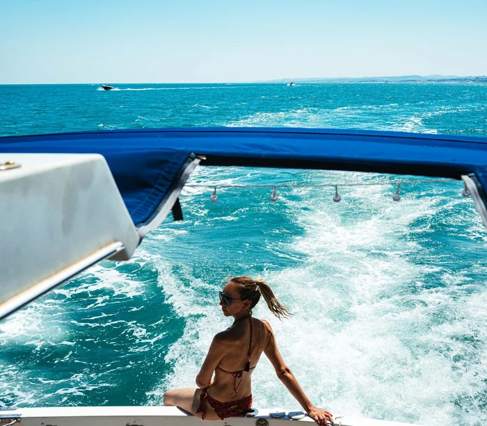 Escursioni in barca al Conero e molto altro Donna in bikini seduta sulla barca con vista mare e scia d'acqua