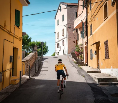 Un family hotel al Conero? Meglio un resort! Ciclista in maglia gialla pedala in salita tra case colorate in un villaggio italiano