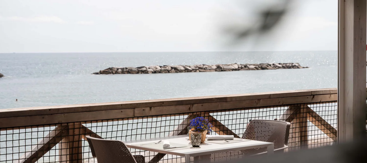 Le specialità culinarie delle Marche e del NVR Tavolo apparecchiato e vista sul mare da una terrazza con balaustra in legno