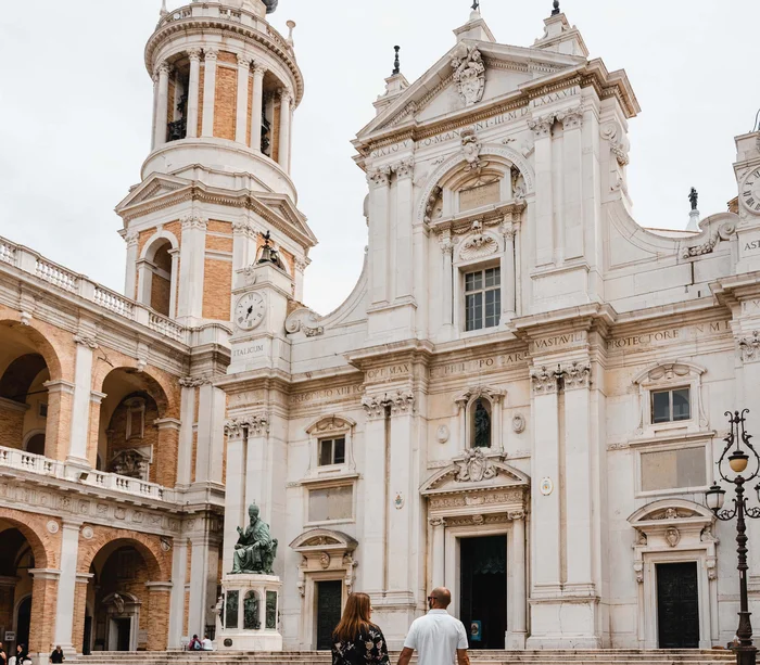 Una vacanza nelle Marche: terra di emozioni Coppia passeggia davanti a una chiesa storica con torre e statua