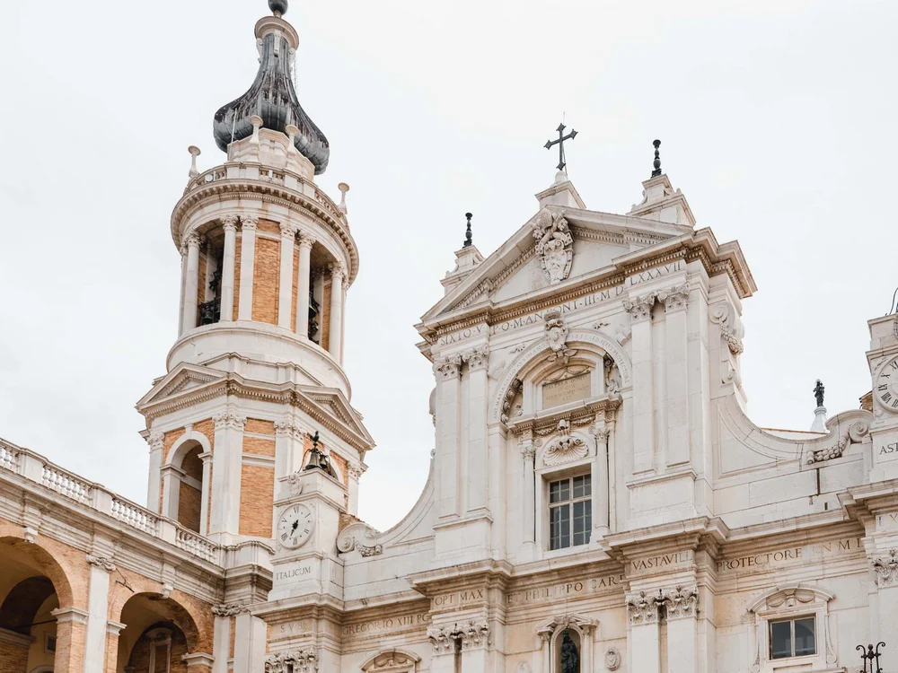 Una vacanza nelle Marche: terra di emozioni Coppia passeggia davanti a una chiesa storica con torre e statua