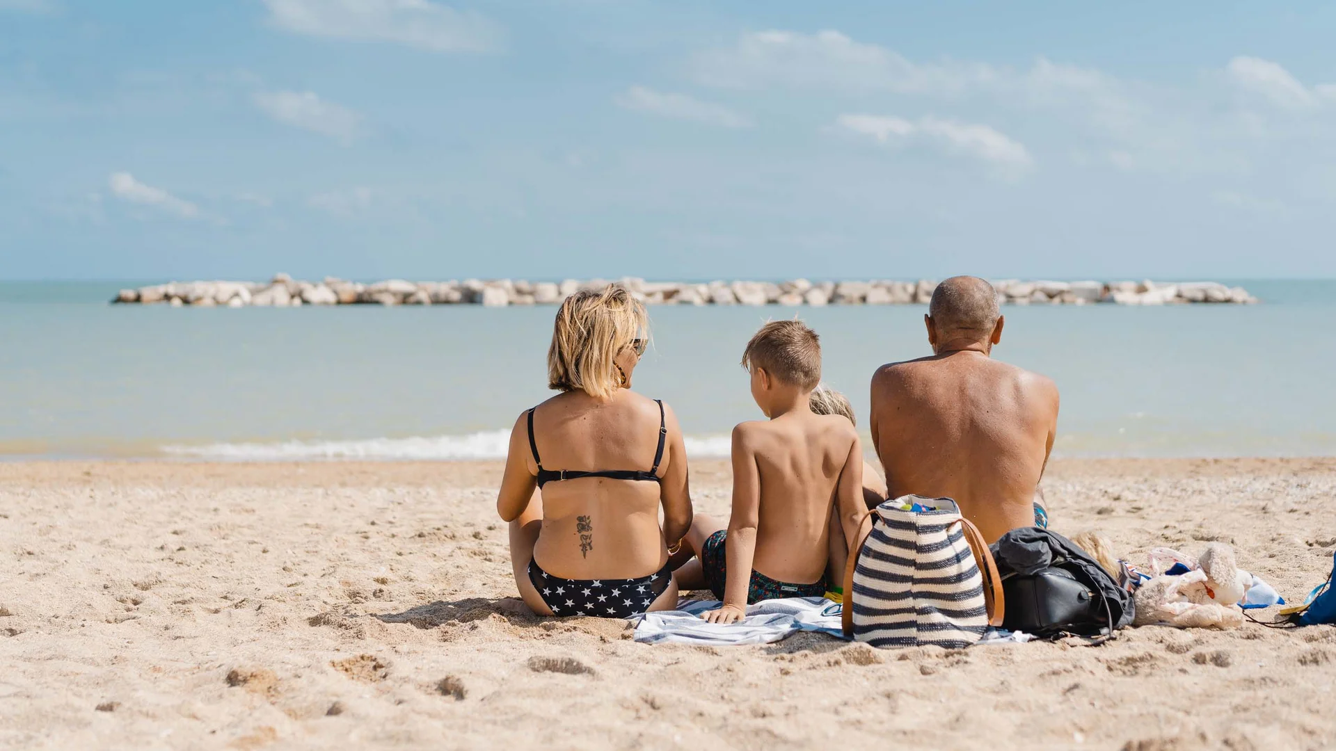 Un resort sul Conero con spiaggia privata Famiglia seduta sulla spiaggia con vista sul mare e scogliere distanti