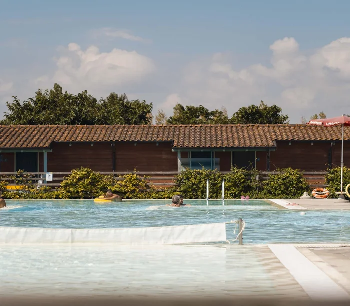 Villaggio nelle Marche sul mare con piscina Piscina all'aperto con bagnanti e casa in legno sullo sfondo sotto il cielo azzurro