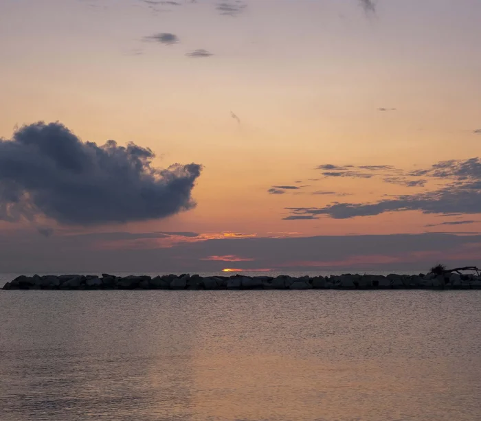 Riviera del Conero: le spiagge più belle Tramonto sul mare con cielo nuvoloso e rocce all'orizzonte