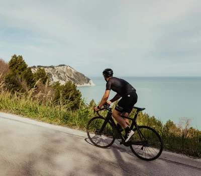 Un family hotel al Conero? Meglio un resort! Ciclista su strada di montagna con vista sul mare e scogliere