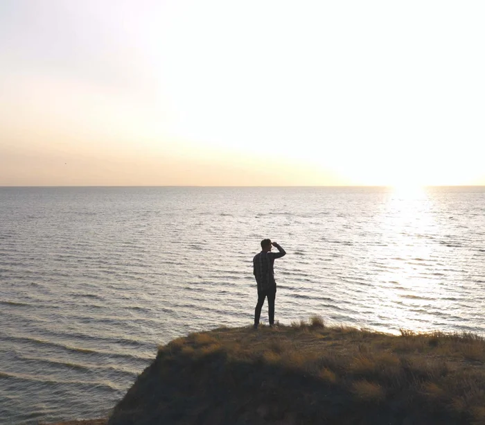 Una vacanza nelle Marche: terra di emozioni Persona in piedi su una scogliera che guarda il tramonto sul mare