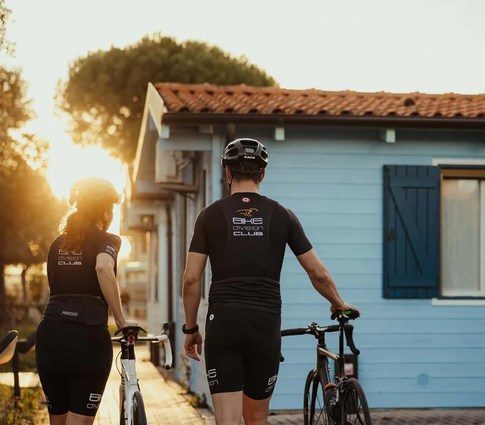 Una vacanza al mare sul Conero Due ciclisti spingono le biciclette verso una casa blu al tramonto