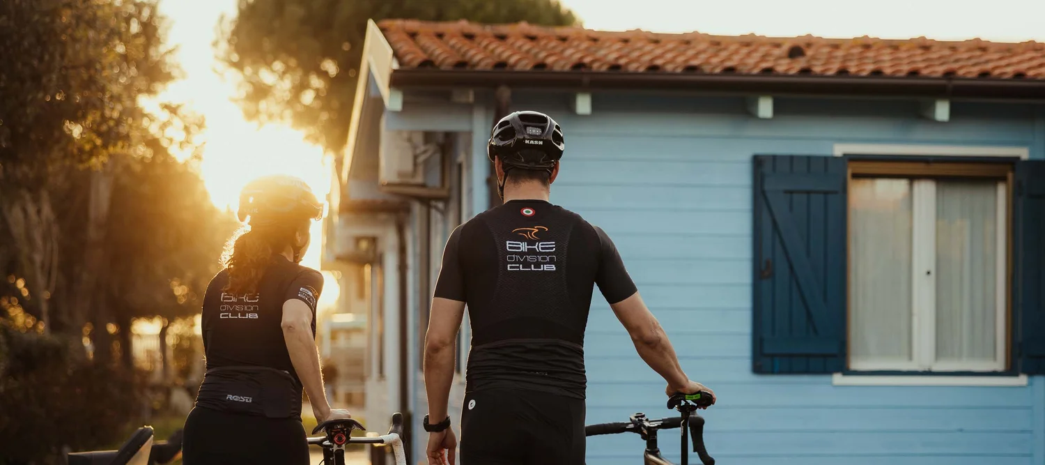 Dai monti al mare: le vostre avventure nelle Marche Due ciclisti spingono le biciclette verso una casa blu al tramonto