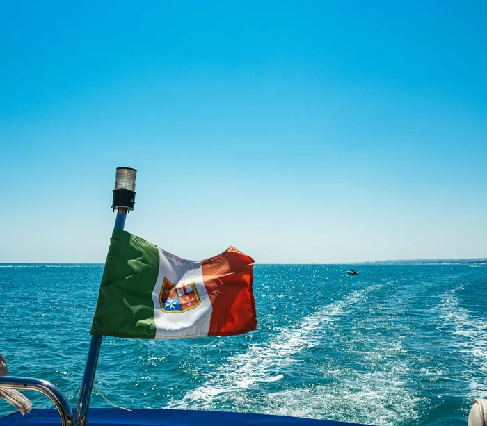 Escursioni in barca al Conero e molto altro Bandiera italiana su una barca che naviga in mare con scia sull'acqua blu