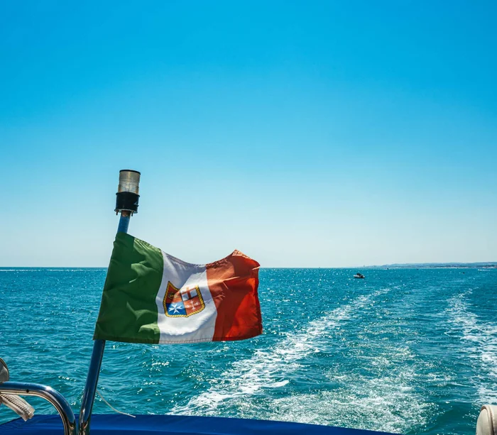 Una vacanza nelle Marche: terra di emozioni Bandiera italiana su una barca che naviga in mare con scia sull'acqua blu