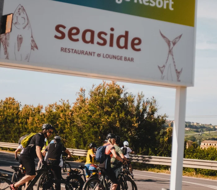 Vacanza in e-bike nelle Marche Gruppo di ciclisti vicino al cartello del ristorante seaside Natural Village Resort