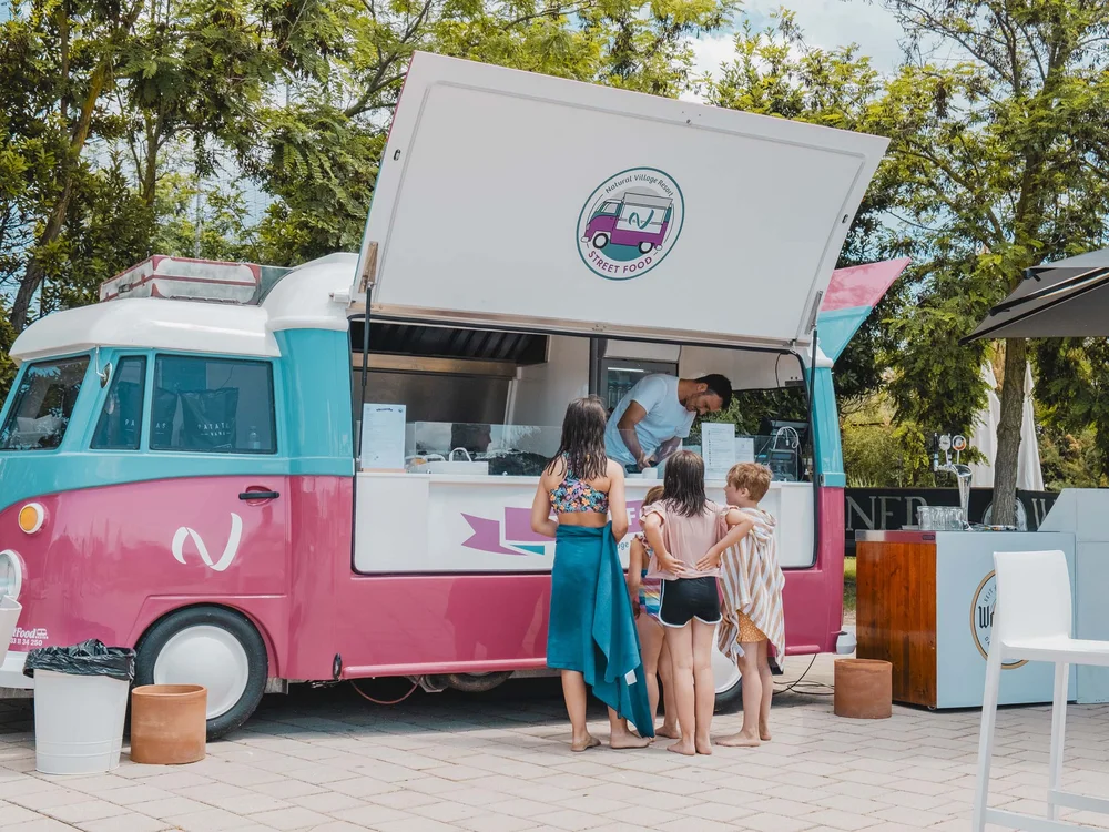 Villaggio nelle Marche sul mare con piscina Bimbi in costume ordinano al food truck rosa e azzurro all'aperto vicino a tavoli