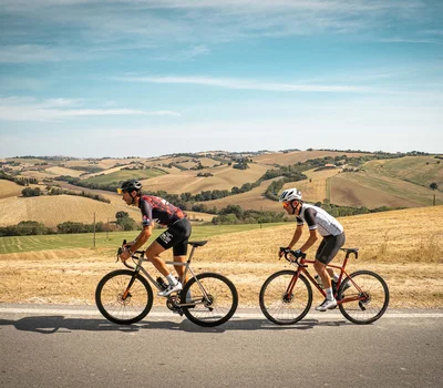 Un family hotel al Conero? Meglio un resort! Due ciclisti su strada pianeggiante con paesaggio collinare arido sullo sfondo