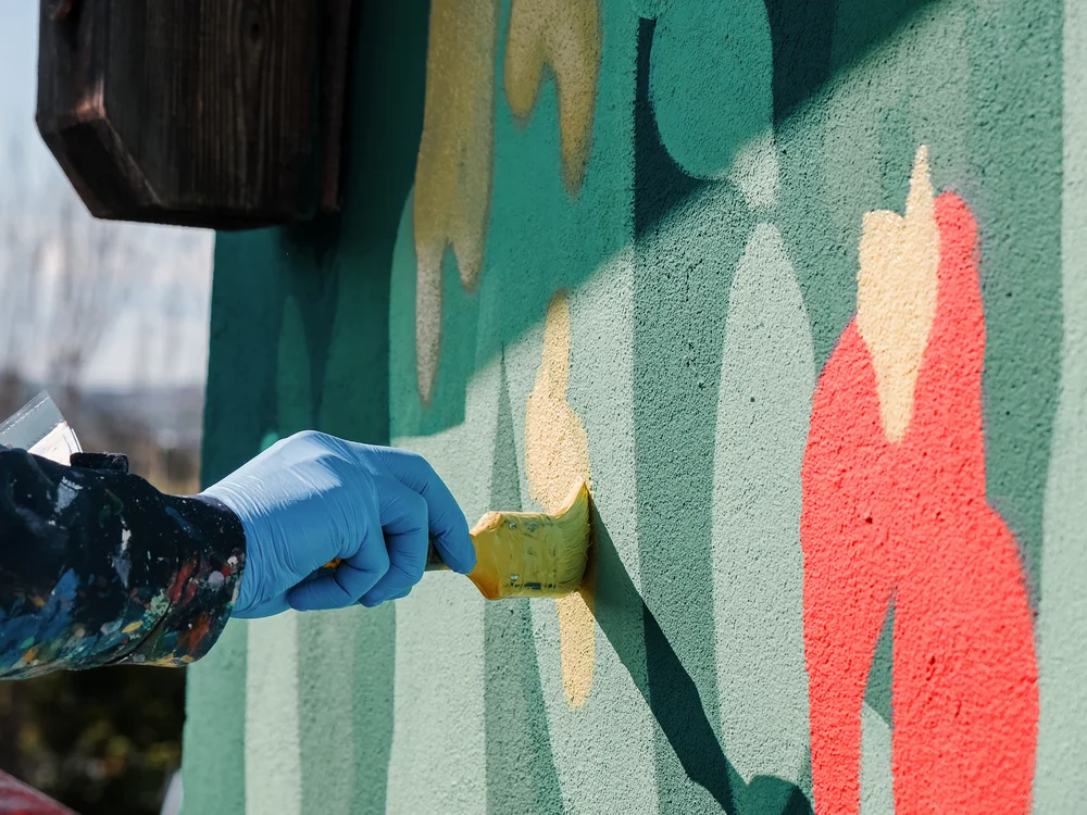 Gli eventi al Natural Village Resort Mano con guanto blu che dipinge un murale colorato con un pennello