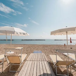 I nostri chalet al mare nelle Marche Lettini e ombrelloni beige su spiaggia sabbiosa con vista sul mare calmo