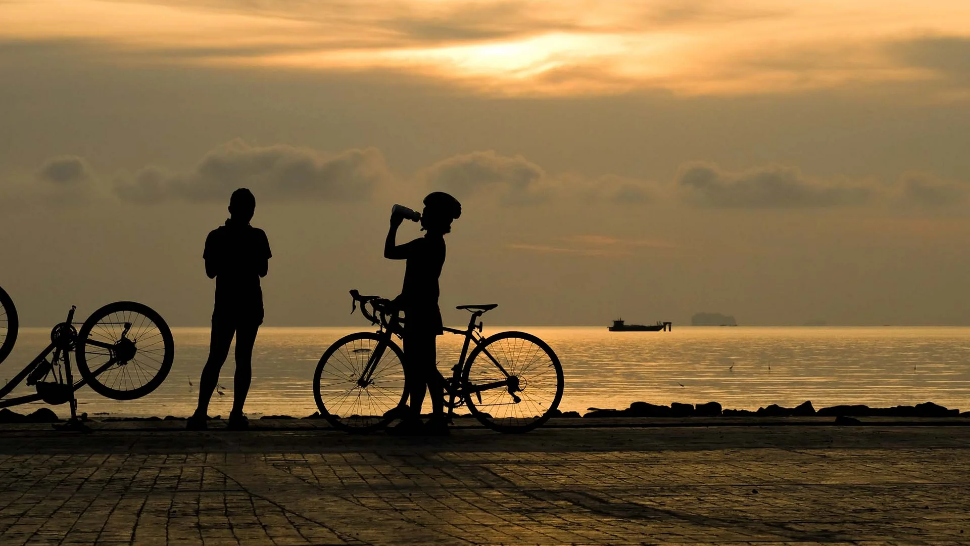 Una vacanza in gravel bike nelle Marche Due ciclisti con biciclette al tramonto presso il mare, uno beve acqua