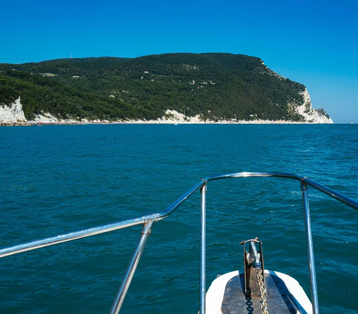 Escursioni in barca al Conero e molto altro Vista dalla prua di una barca verso una costa montuosa verde e mare blu