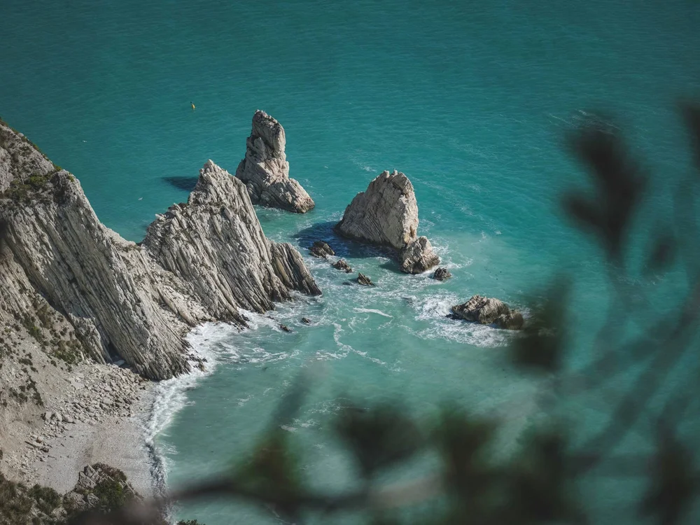 Spiaggia Urbani: la mezzaluna di Sirolo Scogliera rocciosa con acque turchesi e onde sulla costa