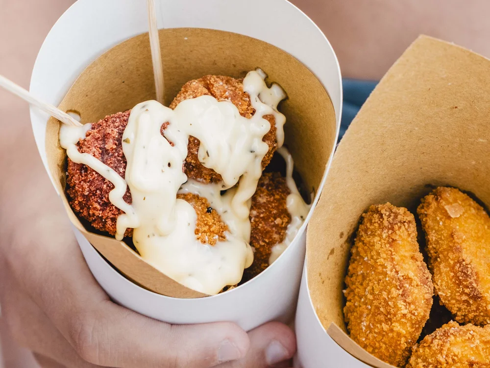 Food truck & Pizzeria a Potenza Picena Mani che tengono crocchette con salsa bianca in bicchieri di carta