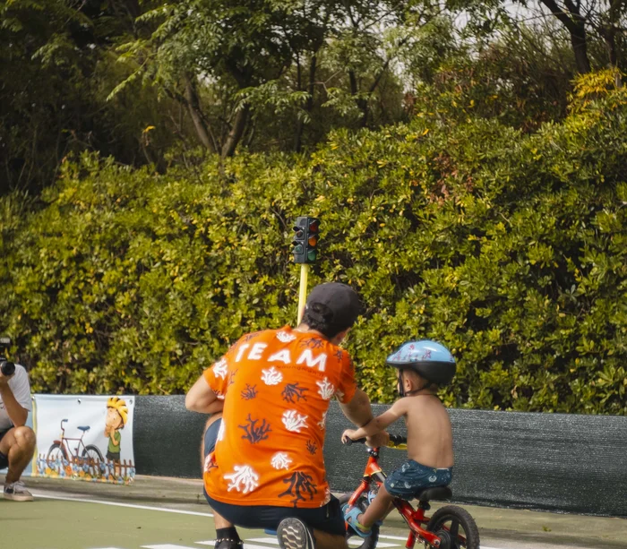 Vacanza in e-bike nelle Marche Bambino con casco impara a andare in bici guidato da adulto con maglia arancione