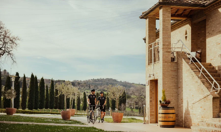 Resort al mare: pronti per un’escursione sul Conero? Ciclisti con bici davanti a casa di campagna vicino a colline e cipressi
