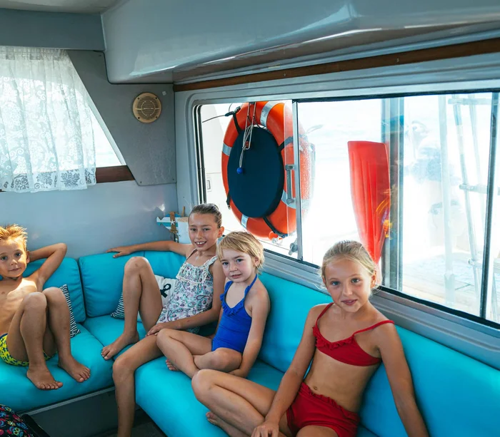 Escursioni in barca al Conero e molto altro Quattro bambini in costumi da bagno seduti su divano blu in barca