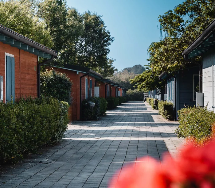 Un villaggio nelle Marche sul mare: il Natural Village Resort Sentiero tra piccole case colorate con vegetazione e alberi sotto cielo sereno