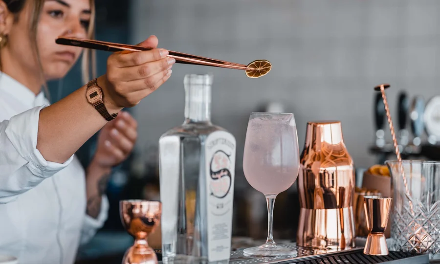 Seaside restaurant & lounge bar in the Marche region Bartender decorating cocktail with dried lemon slice using tongs