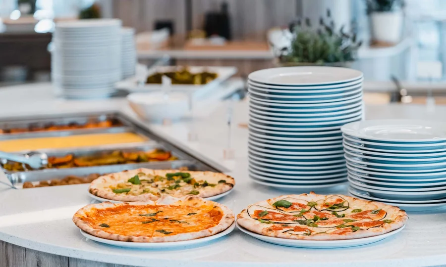 Un villaggio nelle Marche sul mare: il Natural Village Resort Tre pizze su piatti bianchi accanto a una pila di piatti vuoti su un bancone