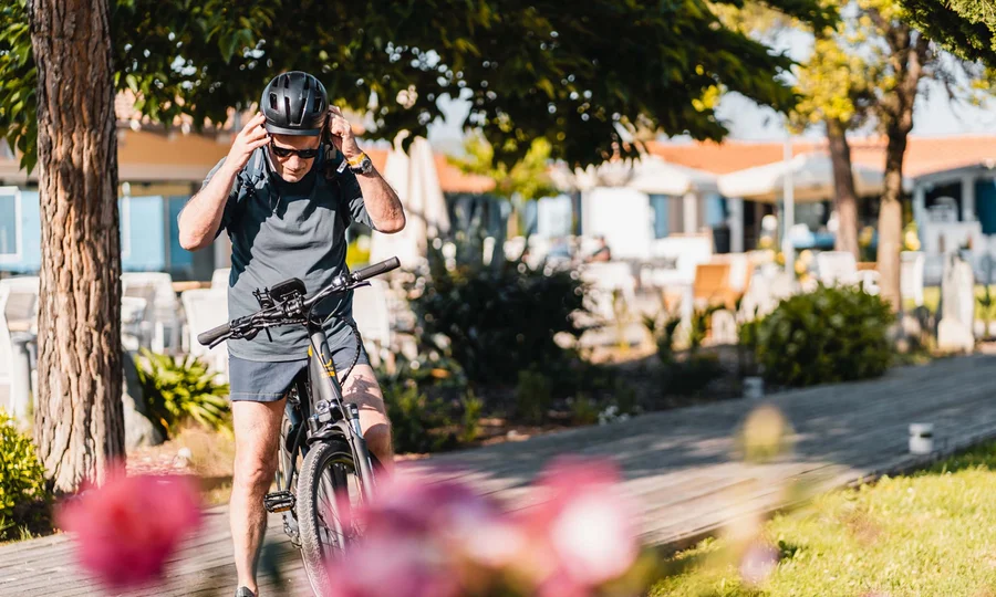 What could be better than a bike hotel in the Marche region? Man putting on helmet preparing to ride bike in sunny park